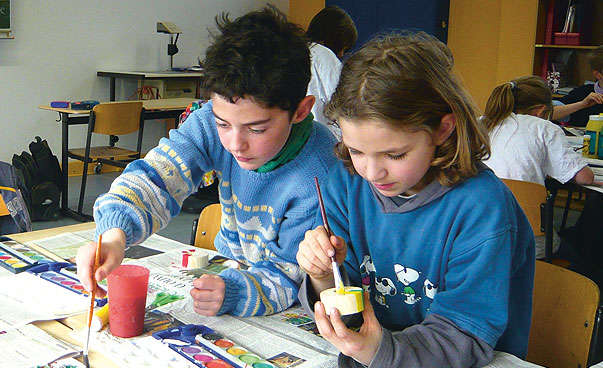 A little girl and a boy are painting in school.