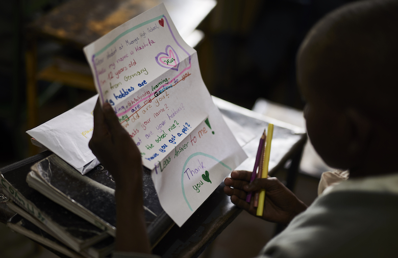 Ein Mädchen sitzt in einem Klassenzimmer am Tisch und liest einen Brief einer Brieffreundin aus einer Schulpartnerschaft.
