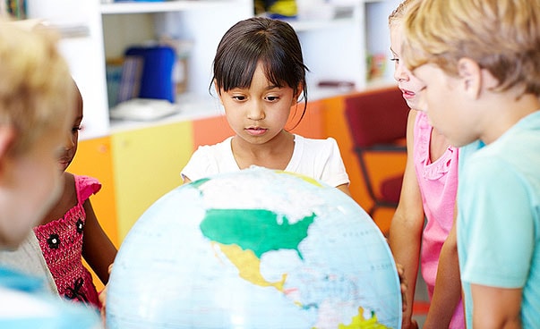 Ein paar Kinder stehen in der Schulklasse um einen Globus versammelt.