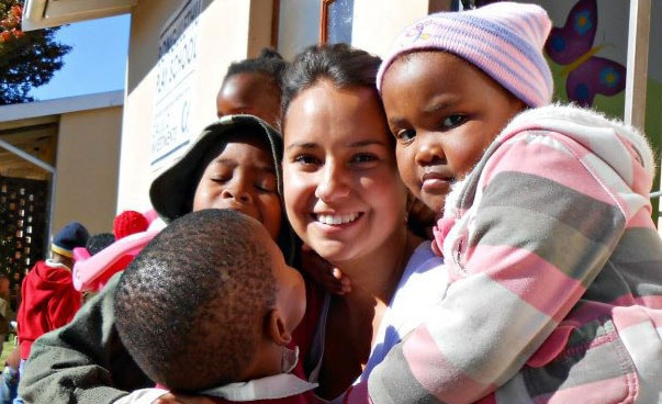 Eine junge Frau ist im Rahmen eines freiwilligen Jahres im Ausland und hält zwei Kinder im Arm.
