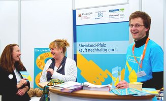 Drei Teilnehmer der Veranstaltung vor einem Plakat mit der Aufschrift "Rheinland-Pfalz kauft nachhaltig ein!".