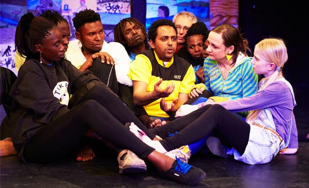 Die Jugendlichen der Theatergruppe sitzen eng beieinander im Kreis auf dem Boden.