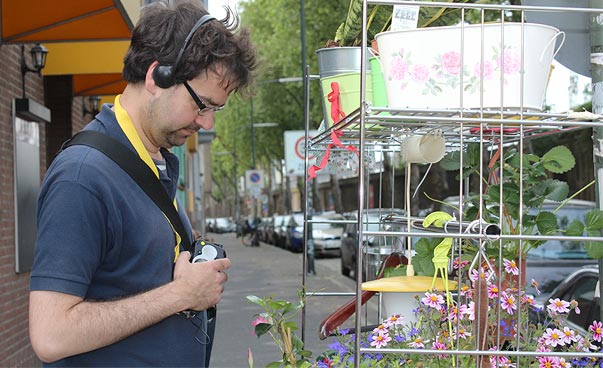 Ein Mann hat Kopfhörer auf und steht auf der Straße vor einem Regal voller Blumen.