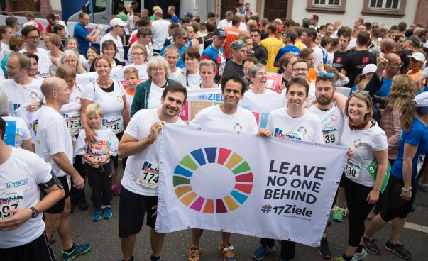 Teilnehmende des Mainzer Firmenlaufs posieren für ein Foto mit einer Flagge mit der Aufschrift „Leave no one behind“. Foto: Engagement Global