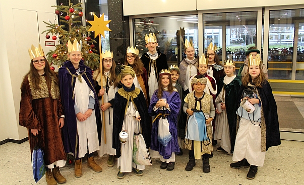 Eine Gruppe von Kindern und Jugendlichen steht vor einem Weihnachtsbaum. Sie tragen Kronen, Sterne und Umhänge.