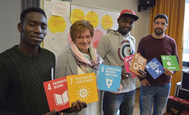 Drei Männer und eine Frau stehen in einer Reihe. In den Händen halten Sie Tafeln mit Aufdrucken der globalen Nachhaltigkeitsziele.