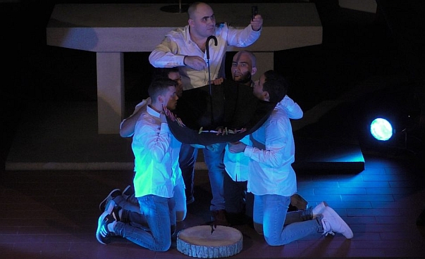 Fünf Männer stehen auf einer Theaterbühne. Sie halten einen Regenschirm.