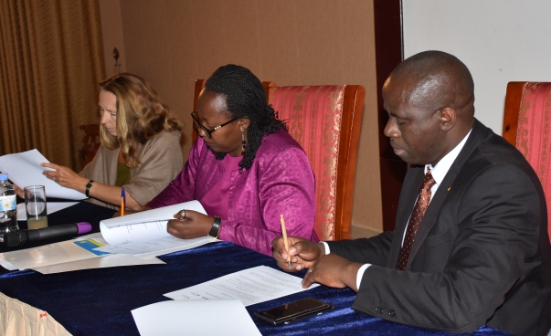 Zwei Frauen und ein Mann sitzen nebeneinander. Sie unterzeichnen Dokumente. Foto: MINALOC Ruanda