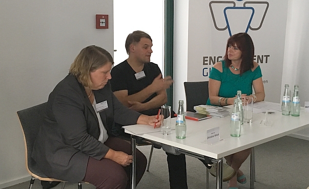 Prof. Dr. Christine Wieck von der Universität Hohenheim, Olaf Bernau, Sozialwissenschaftler sowie die Journalistin und Moderatorin Monika Hoegen, sitzen an einem tisch und reden.