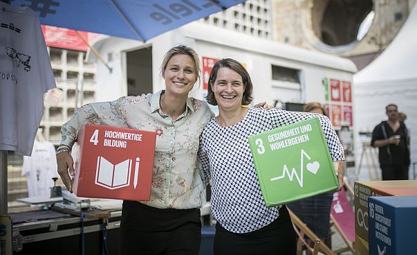 Britta Heidemann, Fecht-Olympiasiegerin und Veronika Rücker, Vorstandsvorsitzende des Deutschen Olympischen Sportbundes, halten zwei der Nachhaltigkeitsziele unter dem Arm.