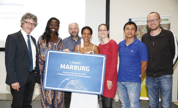 Eine Gruppe von Menschen posiert für ein Foto auf der Bühne. Es sind die Gewinner des Wettbewerbs „Kommune bewegt Welt“ aus Marburg 2016. Foto:Tobias Vollmer
