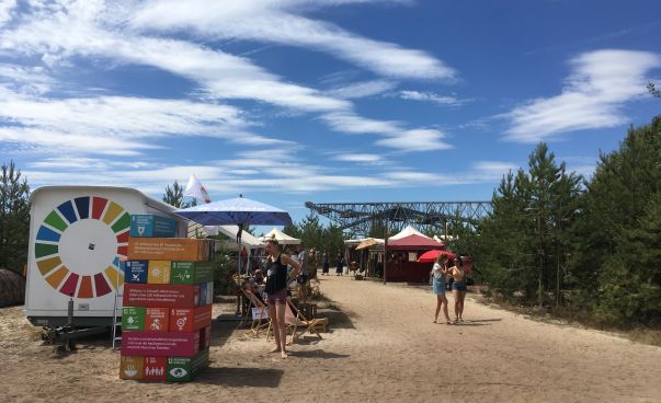 Das 17-Ziele Mobil steht mit Sonnenschirm und bunten Jenga auf dem sandigen Boden des Feel-Festivals. Foto: Engagement Global