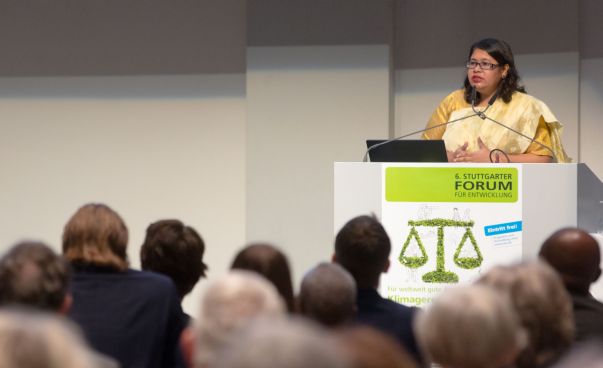Eine Frau steht an einem Rednerpult und spricht zum Publikum. Es ist das Plakat des sechsten Stuttgarter Forums für Entwicklungspolitik zu erkennen. Foto: SEZ/Frank Eppler