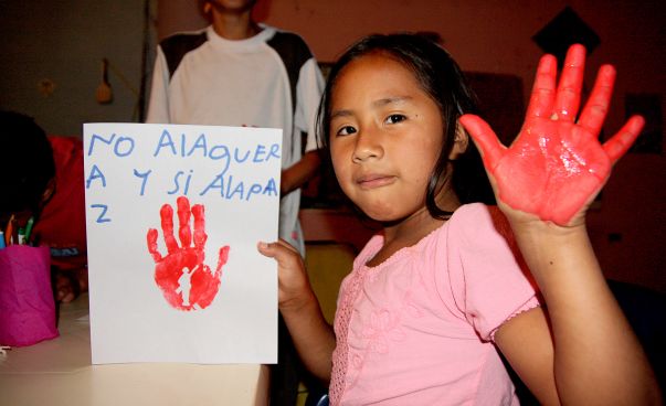 Ein Mädchen zeigt ihre mit roter Farbe bemalte Handfläche in die Kamera. In der anderen Hand hält sie ein Plakat mit ihrem roten Handabdruck. Foto: Simon Bösterling / terre des hommes