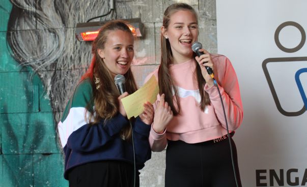 Zwei jungen Mädchen stehen zusammen auf einer Bühne und sprechen in ein Mikrofon. Foto: Engagement Global