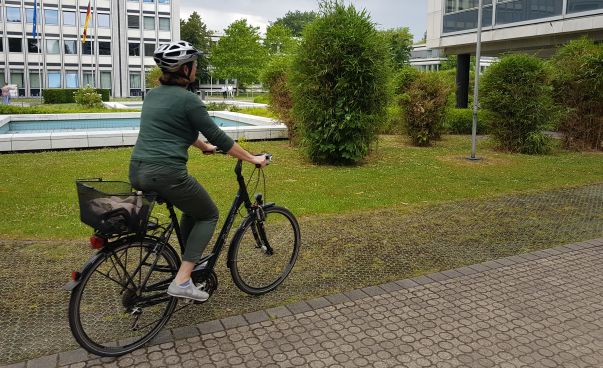 Zu sehen ist eine Frau auf einem Fahrrad in Bonn. Im Hintergrund ist das Gebäude der Bundesnetzagentur zu sehen. Foto: Engagement Global