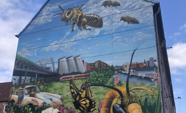 Auf einem Wandbild sind Bienen, eine Blumenwiese und die Skyline einer Stadt zu sehen.