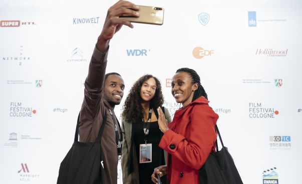 Ein Mann und zwei Frauen machen gemeinsam ein Selfie-Foto vor der Fotowand auf dem Film Festival Cologne. Foto: René Frampe