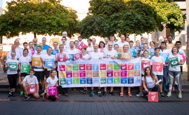 Läuferinnen und Läufer stehen nebeneinander und halten bunte Plakate mit den 17 Zielen für nachhaltige Entwicklung in den Händen. Foto: Kathi Krechting