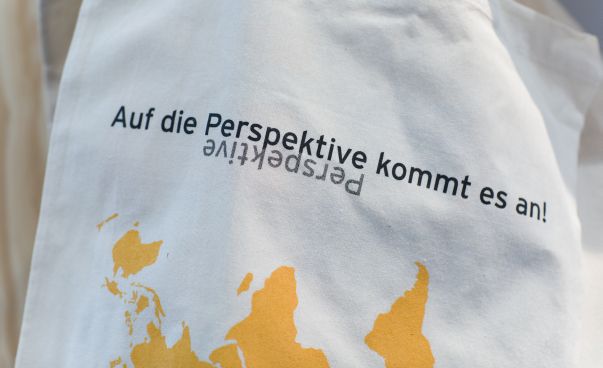 Weißer Stoffbeutel mit der Aufschrift "Auf die Perspektive kommt es an". Darunter ist die Weltkarte auf dem Kopf stehend zu sehen. Foto: Eldar Bock