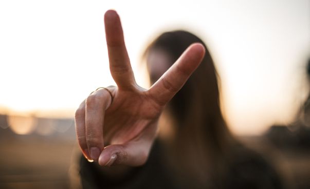 Eine Frau zeigt mit ihren Fingern das Peace-Zeichen. Foto: Priscilla du Preez
