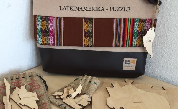 Auf einem Tisch liegen Puzzleteile in der Form verschiedener lateinamerikanischer Länder. Dahinter steht eine Umhängetasche. Foto: Engagement Global
