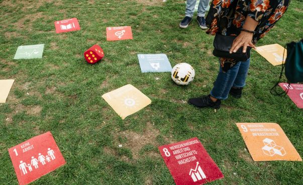 Auf einer Wiese liegen bunte Quadrate mit den 17 Zielen für nachhaltige Entwicklung und ein Fußball.