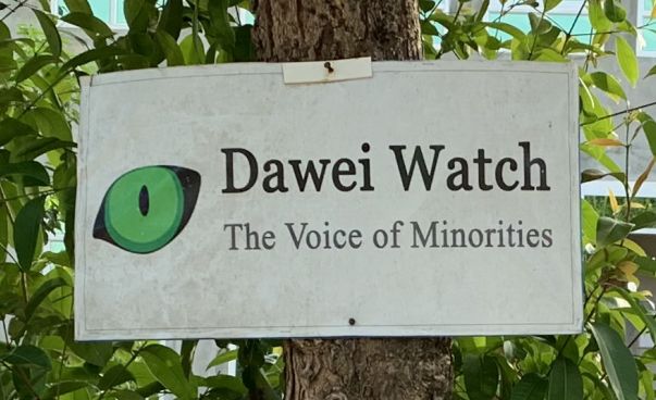 Ein Plakat mit dem Logo von Dawei Watch, einem grünen Auge, hängt an einem Baum. Foto: Dawei Watch