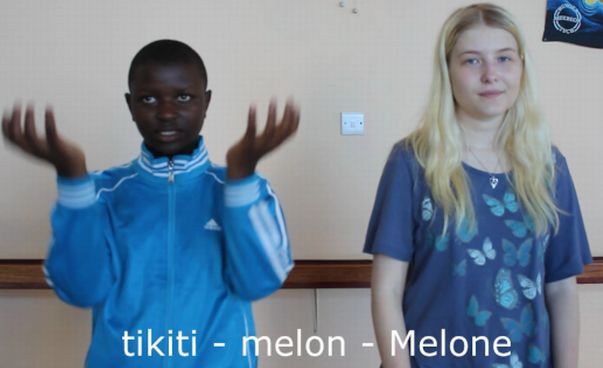 Zwei Kinder stehen nebeneinader und schauen in die Kamera, der Junge gestikuliert. Unten im Bild steht in drei Sprachen Melone.
