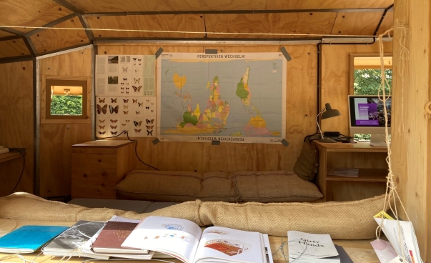 Raum mit Holzverkleidung und Sitzecke, über der unter anderem eine Weltkarte hängt. Diese hängt "auf dem Kopf".