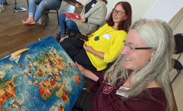 Eine Frau in einem Stuhlkreis betrachtet einen Adventskalender auf dem eine farbenfrohe Weltkarte abgebildet ist.