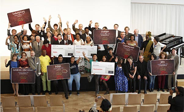 Das Foto zweigt alle Siegerinnen und Sieger der Preisverleihung von 2014 auf einer Bühne mit winkenden Händen.