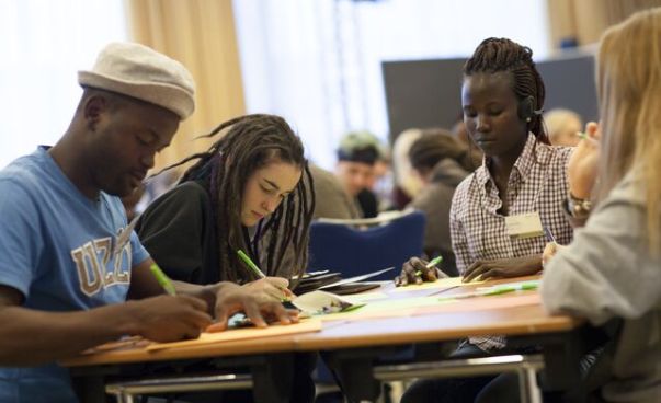 Drei junge Menschen sitzen am Tisch und schreiben. Foto: Engagement Global/Dave Grossmann