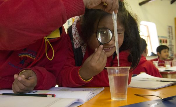Ein Mädchen schaut durch eine Lupe. Ein anderes Kind tropft mit einer Pipette Flüssigkeit in einen Becher. Foto: Uli Reinhardt / Zeitenspiegel/ Siemens Stiftung
