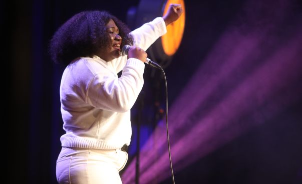 Eine junge Frau in weißer Kleidung singt auf einer Bühne.