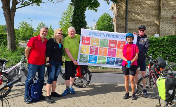 Fünf Personen in Fahrradkleidung halten ein Banner zu den Nachhaltigkeitszielen hoch.