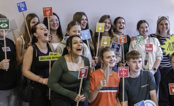 Eine Gruppe junger Menschen hält Schilder mit den 17 Ziele für nachhaltige Entwicklung hoch und lacht.