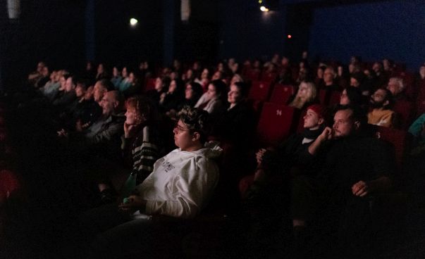 Eine Gruppe von Menschen sitzt in einem dunklen Kino und schaut auf die Leinwand.