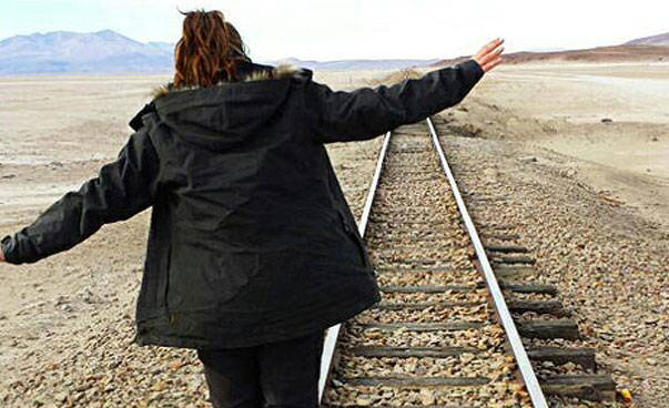 Eine Jugendliche balanciert auf einer Bahngleisschiene.