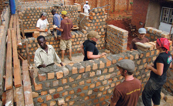 Hauswände aus Stein und Mörtel werden von vielen Helfern gebaut.