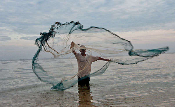 Fischer mit Fischernetz im Wasser stehend.