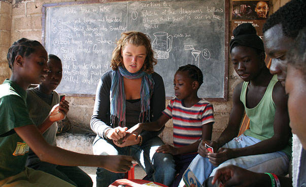Eine junge deutsche Frau sitzt in einer Klasse mit afrikanischen Kindern.